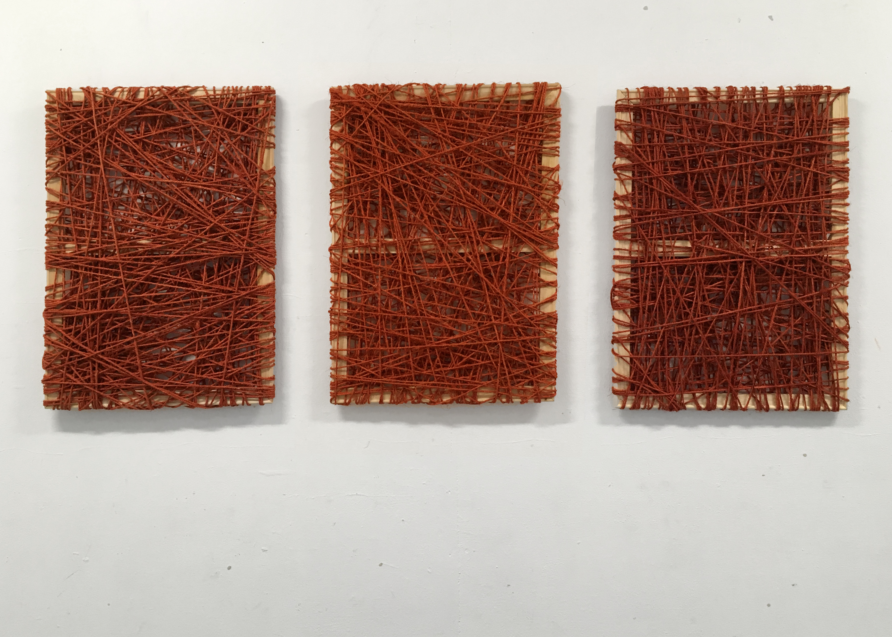 three wooden frames wrapped with red ropes around each one of them on a white wall